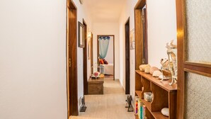 Un pasillo estrecho con puertas de madera, una cama con dosel azul y un estante con adornos.