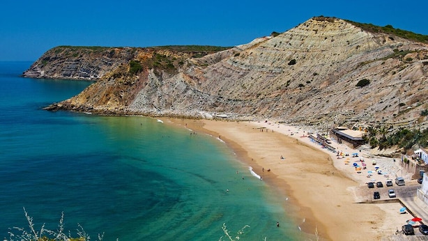 Una playa costera con aguas turquesas cristalinas, una orilla arenosa y un acantilado rocoso.