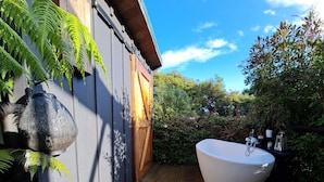 Una terraza de madera con una bañera blanca grande, una maceta rústica y una cerca de madera.