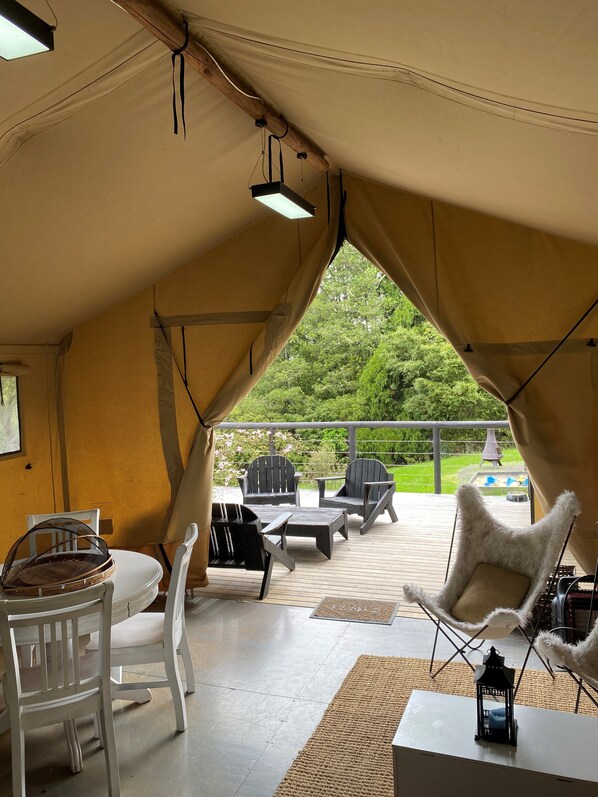 A tented outdoor area with a table and chairs, a lantern, and a view of a garden and pool.