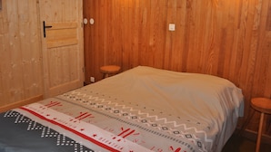 A room with wooden walls, a bed with patterned bedding, two wall-mounted lights, and a door with a handle. - Quiet chalet in Abondance, 4 bedrooms, fireplace (Abondance)
