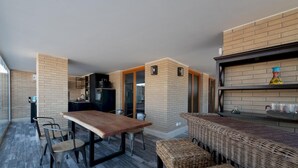 A compact kitchen with a dining area, a wicker bench, and a built-in shelf with decorative items.