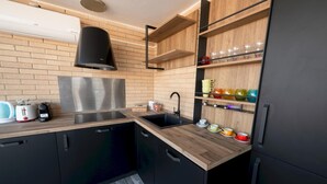 A modern kitchen with black cabinets, a wooden countertop, a stainless steel range hood, and a built-in shelf with colorful glassware.