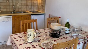 Keittiössä on puukehikoiset kaapit, Bosch-astianpesukone, jääkaappi ja ruokailutila, jossa on pöytä kahdelle.