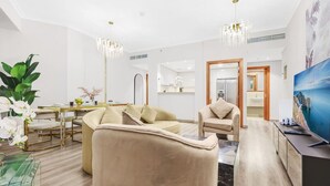 Un soggiorno moderno con un divano beige, un tavolino in vetro, un'area pranzo con tavolo e sedie dorati, e un grande quadro appeso alla parete.