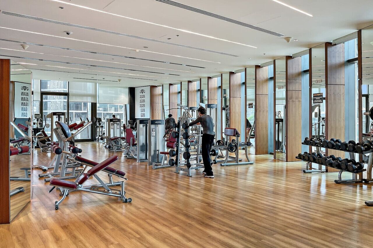 Un gimnasio moderno con diversos equipos de ejercicio, amplias ventanas y un suelo de madera pulida.