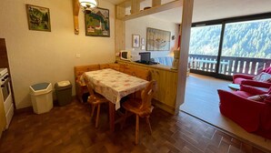 A cozy kitchen with wooden furniture, a dining table, and a view of a snowy forest through large windows. - Spacious studio near center and lift with parking (Châtel)