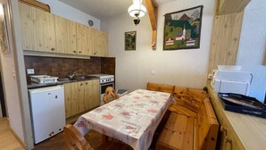 A compact kitchen with wooden cabinets, a white refrigerator, a stove, and a dining table with a tablecloth. - Spacious studio near center and lift with parking (Châtel)