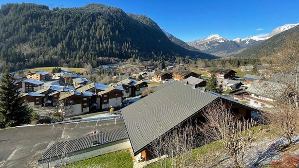 A mountain village with traditional wooden houses, a clear sky, and snow-capped mountains in the background. - Spacious studio near center and lift with parking (Châtel)
