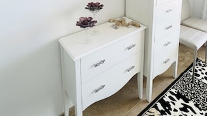 A white dresser with drawers and a mirror, a decorative wall piece, and a small table with a bottle and a glass. - Apartment with sea views in a quiet area (Alcorrín)