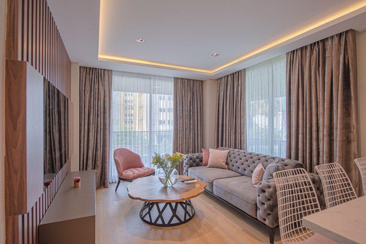 Un salon moderne avec un canapé gris, un fauteuil rose et une table basse en bois sur laquelle est posé un vase.