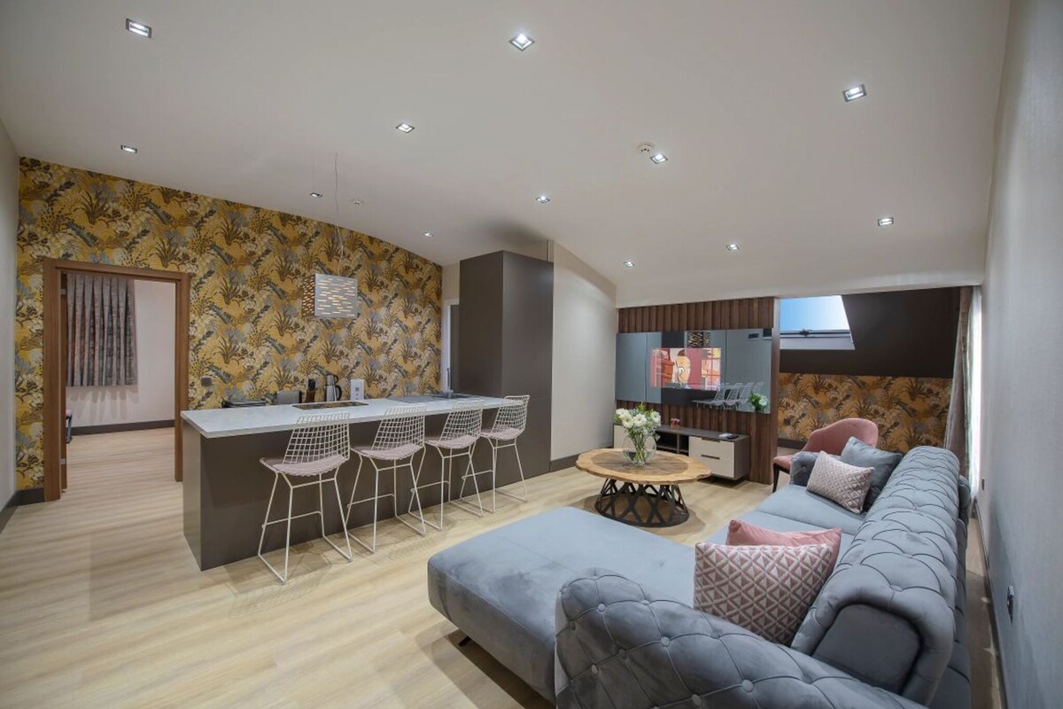 Un salon moderne avec un canapé gris, un coin repas avec une petite table et des chaises, et un espace cuisine avec un bar.