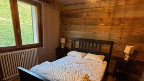 Un dormitorio con cabecera de madera, un ventanal grande, un radiador y una mesita de noche con lámpara.