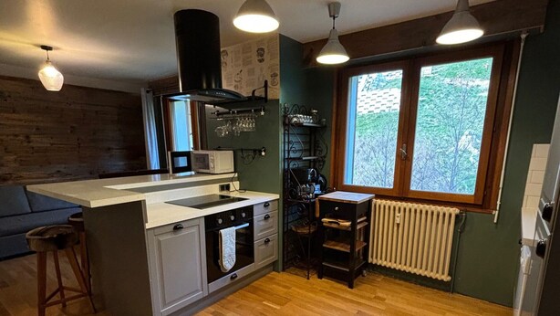Una cocina compacta con una isla central, horno empotrado, microondas y ventana con vistas a árboles.