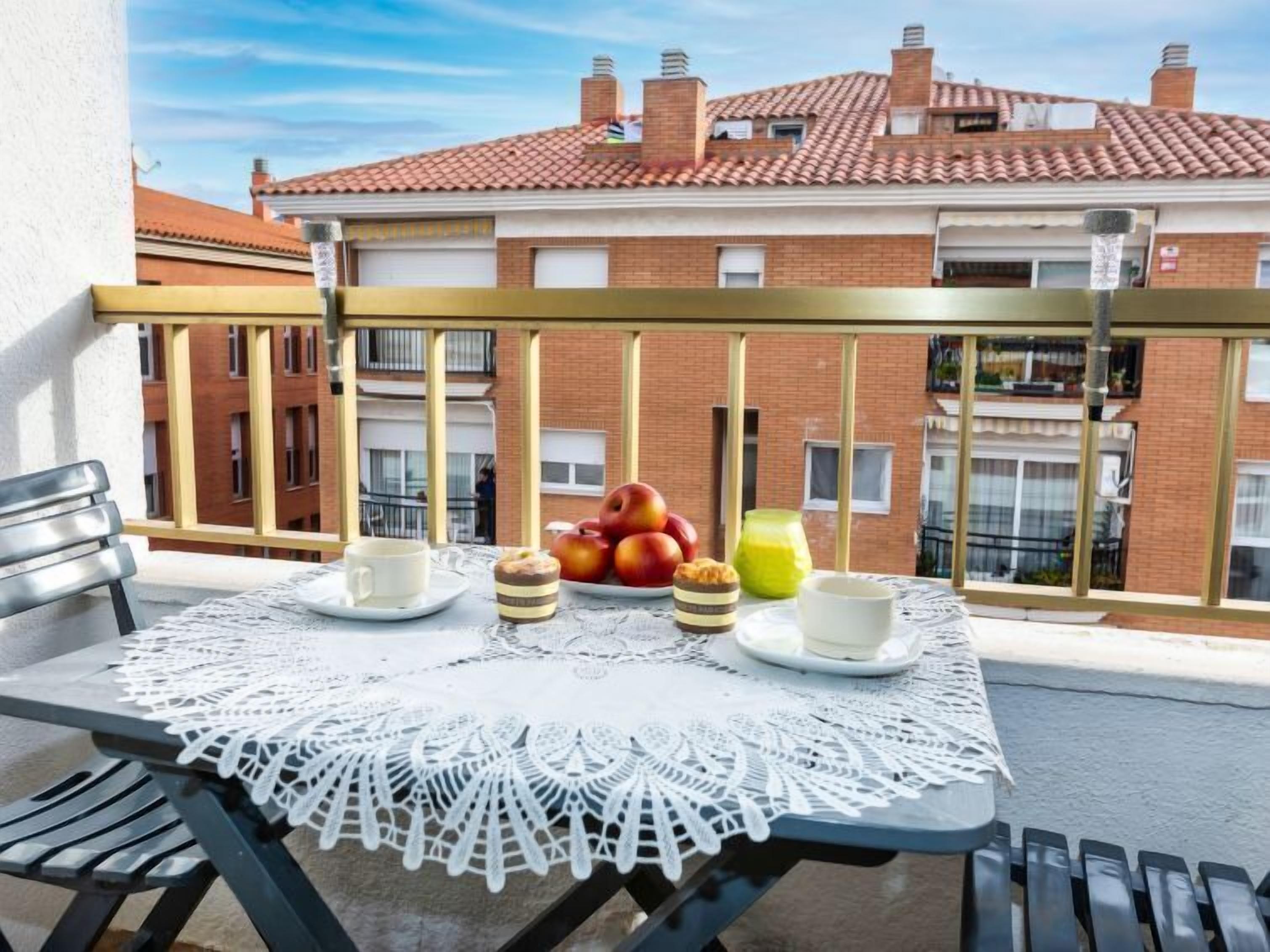 A balcony with a table set for breakfast, including apples, a glass of juice, and pastries.