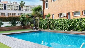 Et rektangulært swimmingpool med en træterrasse, omgivet af en murstensbygning og frodig vegetation.