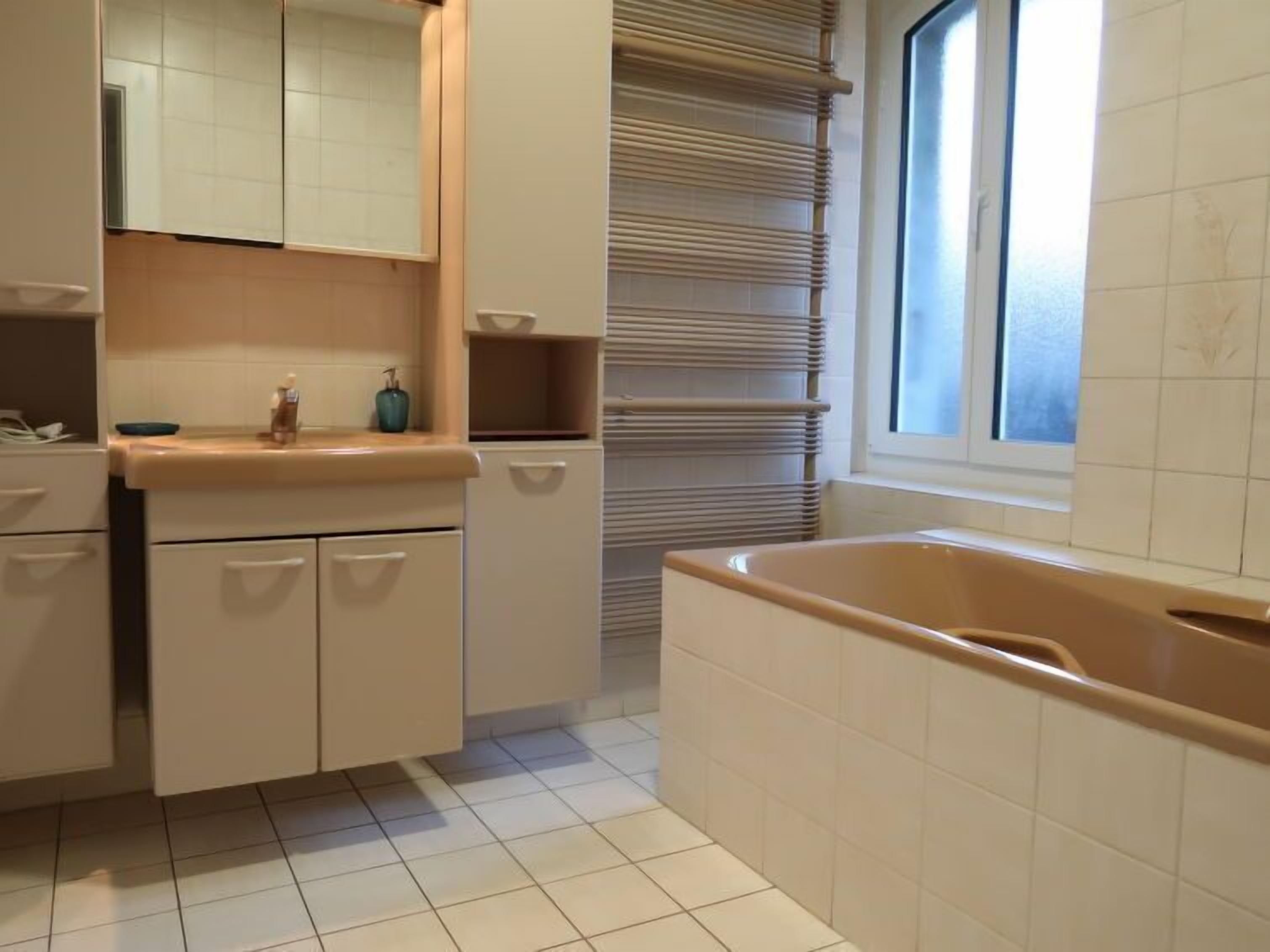 A modern bathroom with a large bathtub, a mirror above the sink, and a window providing natural light.