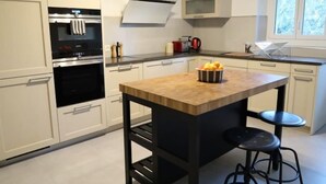 Une cuisine moderne avec des meubles blancs, un îlot central doté de tabourets et une fenêtre donnant sur la verdure.