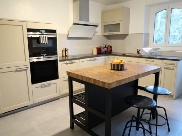 A modern kitchen with white cabinetry, a central island with stools, and a window with a view of trees.