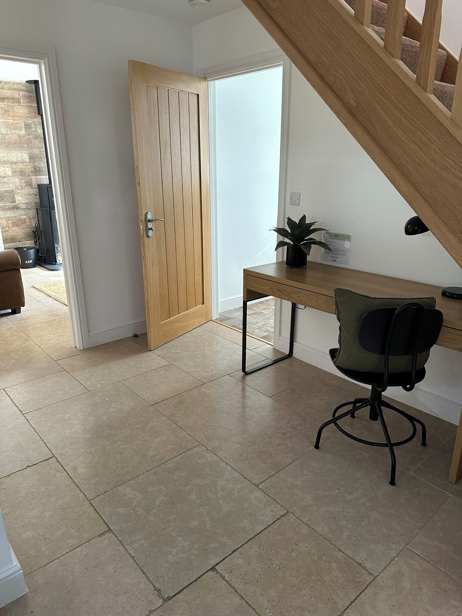 A room with a wooden door, a desk with a chair, and a staircase.