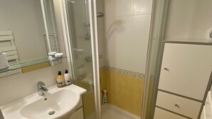 Une salle de bain avec une douche à parois de verre, un lavabo avec un miroir et un petit meuble de rangement.