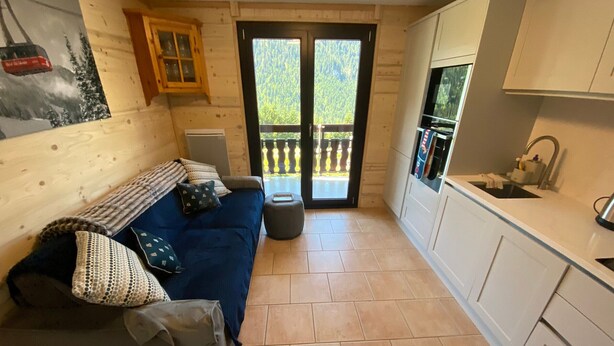 Un intérieur de chalet chaleureux avec un canapé, un coin cuisine et une porte donnant sur un balcon.