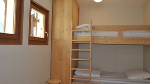 Kerrossängyllä varustettu huone, jossa on puinen tikapuu, ikkuna ja patteri.