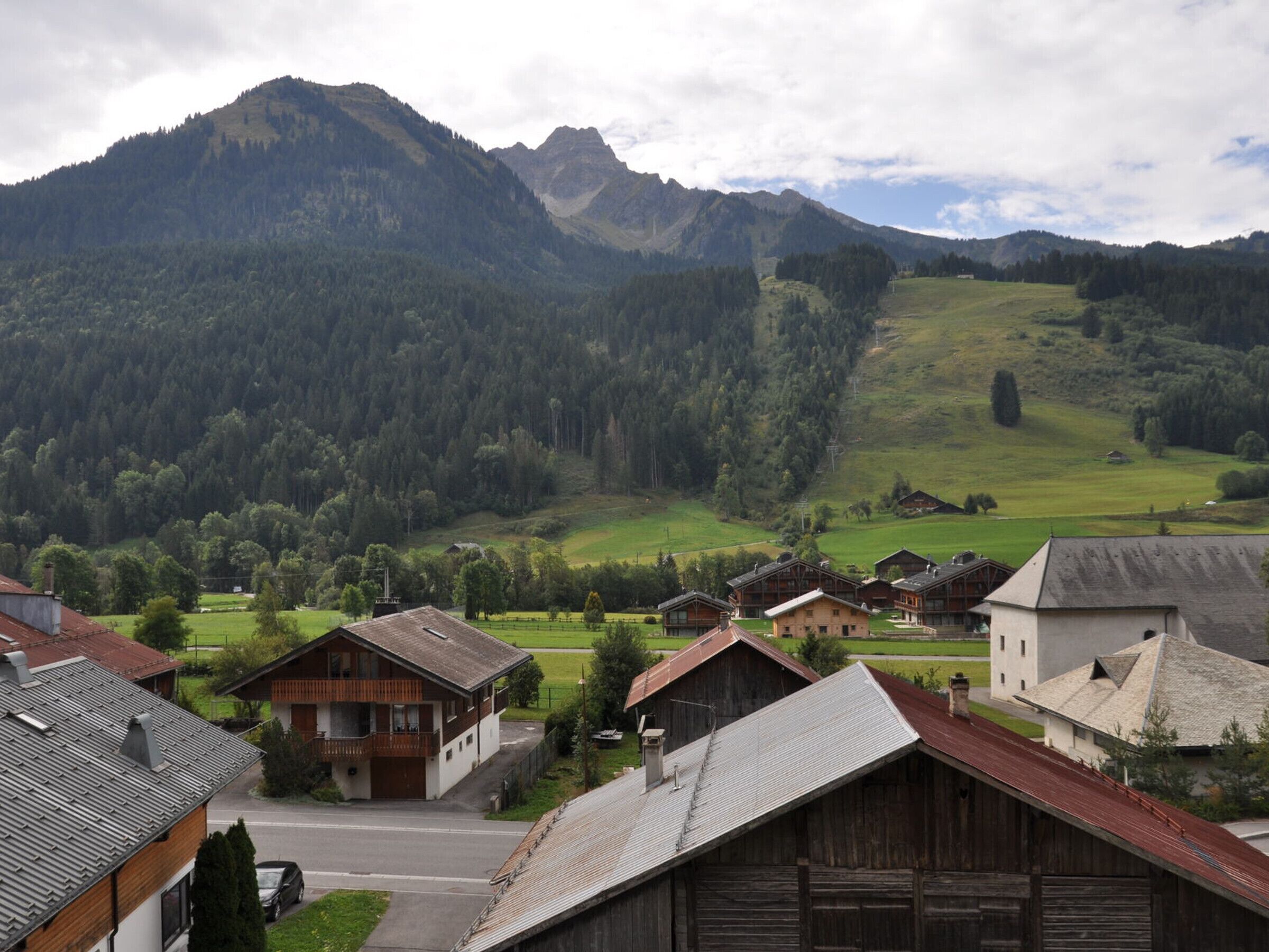 Un village rural avec des maisons traditionnelles en bois, un paysage montagneux en toile de fond et un ciel dégagé.