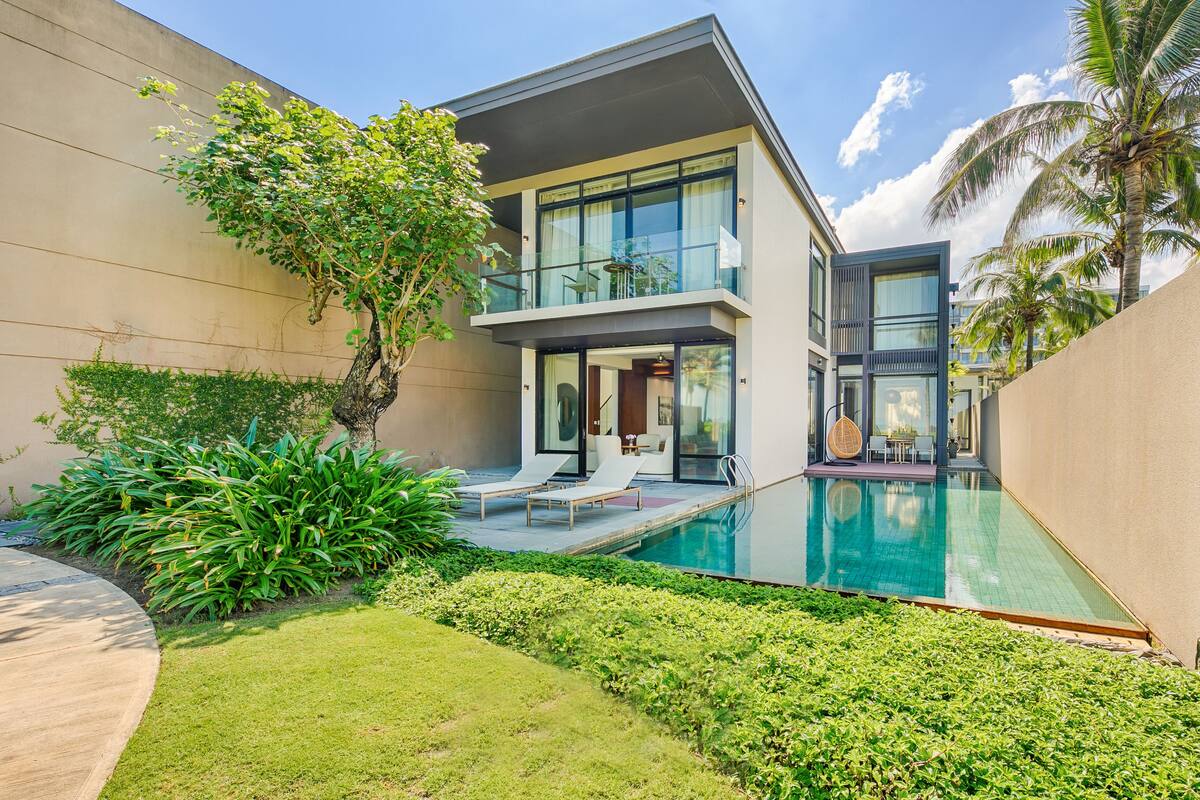 A modern two-story house with a swimming pool, a balcony, and lush greenery.