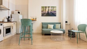 A modern kitchen with white appliances, a dining area with a round table and chairs, a sofa with cushions, and a large framed picture on the wall. - Central Málaga Apartment: Bright, Comfortable, Fully Equipped, Near Attractions (Málaga)
