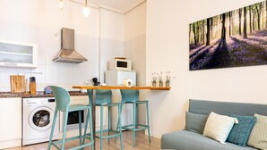 A compact living space with a kitchenette, a dining area with bar stools, a sofa, and a round coffee table. - Central Málaga Apartment: Bright, Comfortable, Fully Equipped, Near Attractions (Málaga)