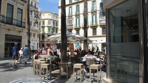 An outdoor café area with tables and chairs, surrounded by buildings with balconies and large windows. - Central Málaga Apartment: Bright, Comfortable, Fully Equipped, Near Attractions (Málaga)
