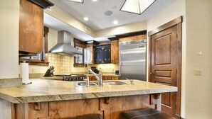 Una cocina con encimeras de granito, electrodomésticos de acero inoxidable, armarios de madera y un taburete de bar.