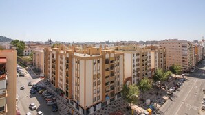 A high-rise residential building with multiple balconies, a parking lot, and a clear view of the cityscape in the background.