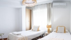 A hotel room with two beds, a checkered floor, a hanging lamp, and an air conditioning unit.