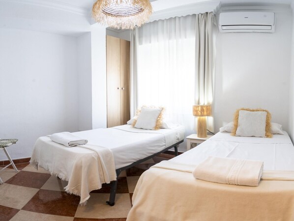Une chambre d’hôtel avec deux lits, un sol à carreaux, une lampe suspendue et un appareil de climatisation.