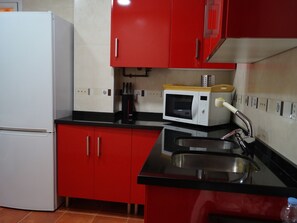 Eine Küche mit roten Schränken, einem weißen Kühlschrank, einer Mikrowelle und einer Spüle aus Edelstahl.