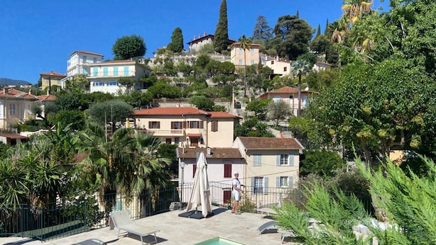 Zona de piscina con sillas de descanso, salvavidas de servicio y vistas a edificios en la colina.