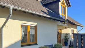 Ein Haus mit Ziegeldach, einem Fenster mit Vorhang, einer Bank und Blumentöpfen.