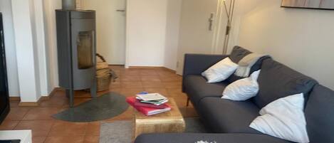 Ett vardagsrum med en soffa, ett litet bord, en öppen spis och en lampa.