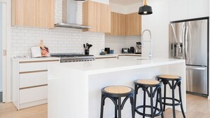 A modern kitchen with a central island, wooden cabinets, white subway tiles, stainless steel appliances, and black bar stools. - Moonah Retreat - 4pm check out Sundays* (Fingal)