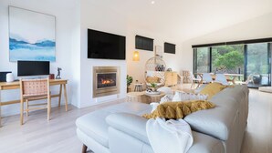 A modern living room with a fireplace, a large sofa, a dining area, and a TV mounted on the wall. - Moonah Retreat - 4pm check out Sundays* (Fingal)