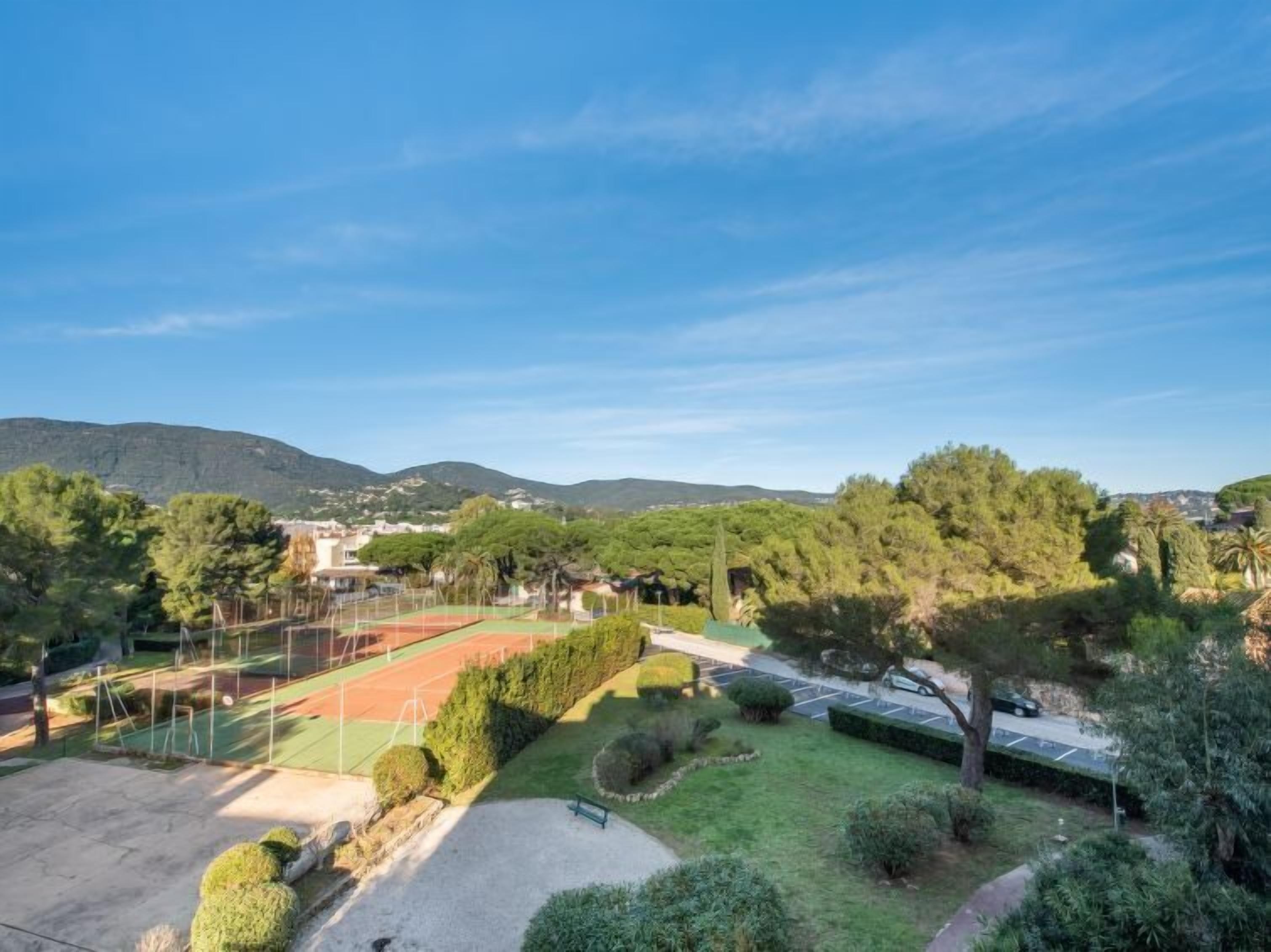 A tennis court surrounded by greenery and hills in the background.