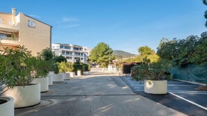 Ein Parkplatz mit Kübelpflanzen, ein Gebäude mit Balkonen und ein klarer Himmel.