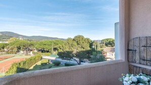 Ein Balkon mit Blick auf einen Tennisplatz, Grünflächen und sanfte Hügel in der Ferne.