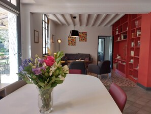 A modern living room with a white table, a vase of flowers, a grey sofa, and a red bookshelf.