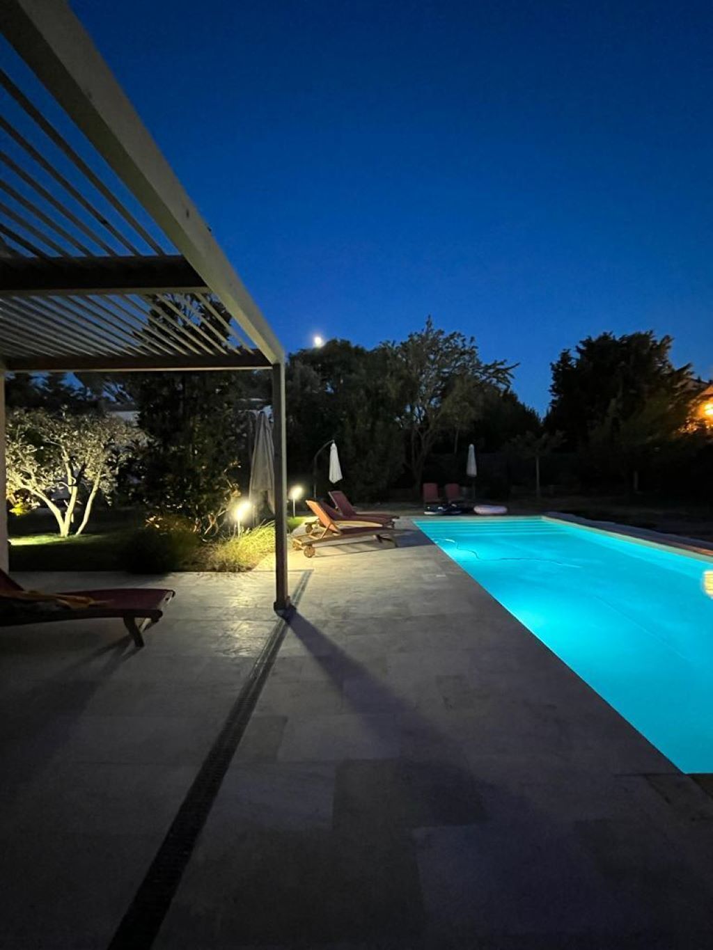 Une piscine dotée de chaises longues et d’un espace abrité éclairé.