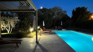 En pool med solstolar och ett överbyggt område med belysning.