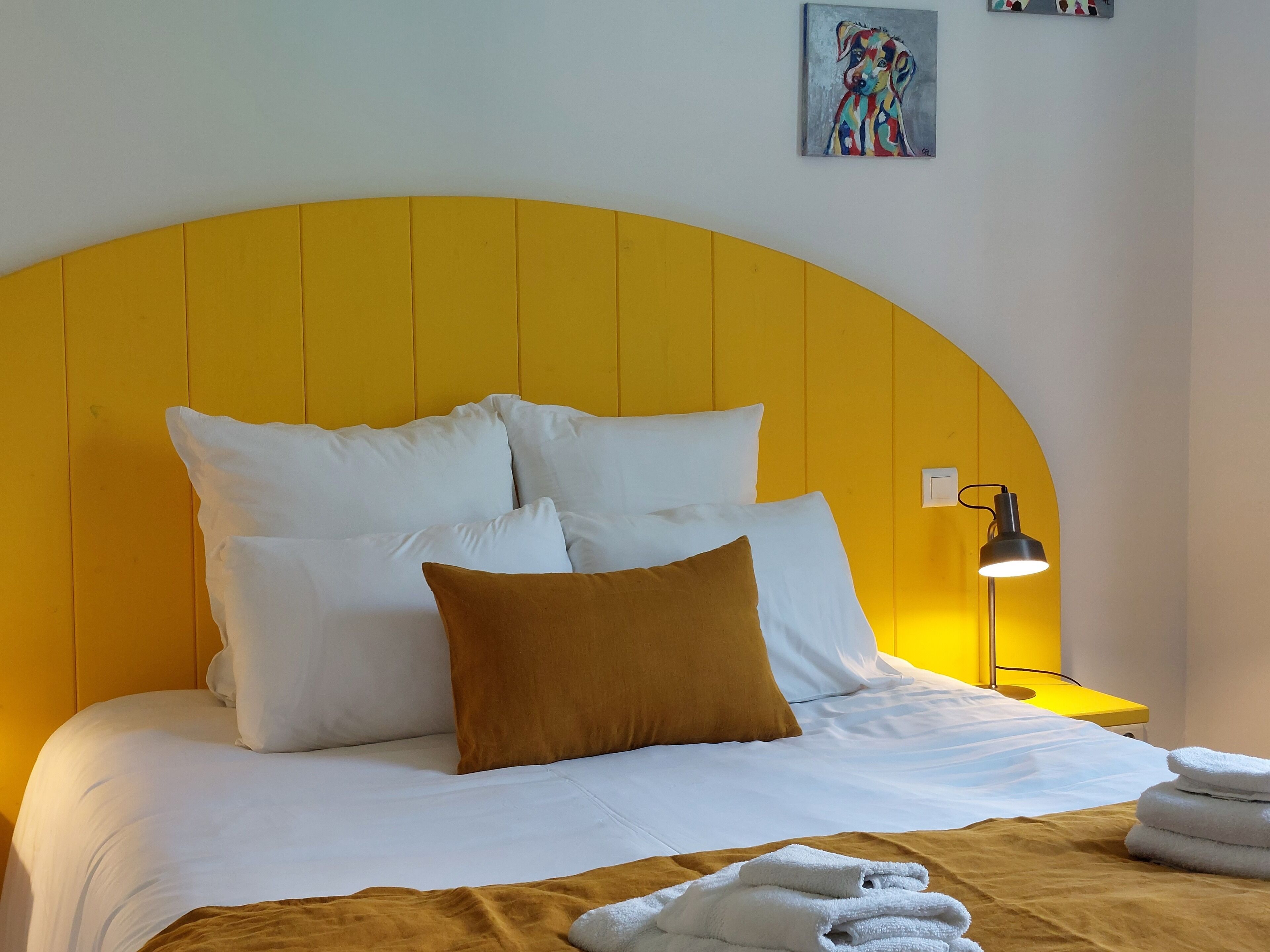 Un lit avec une literie blanche et marron, une tête de lit jaune et une lampe de chevet.