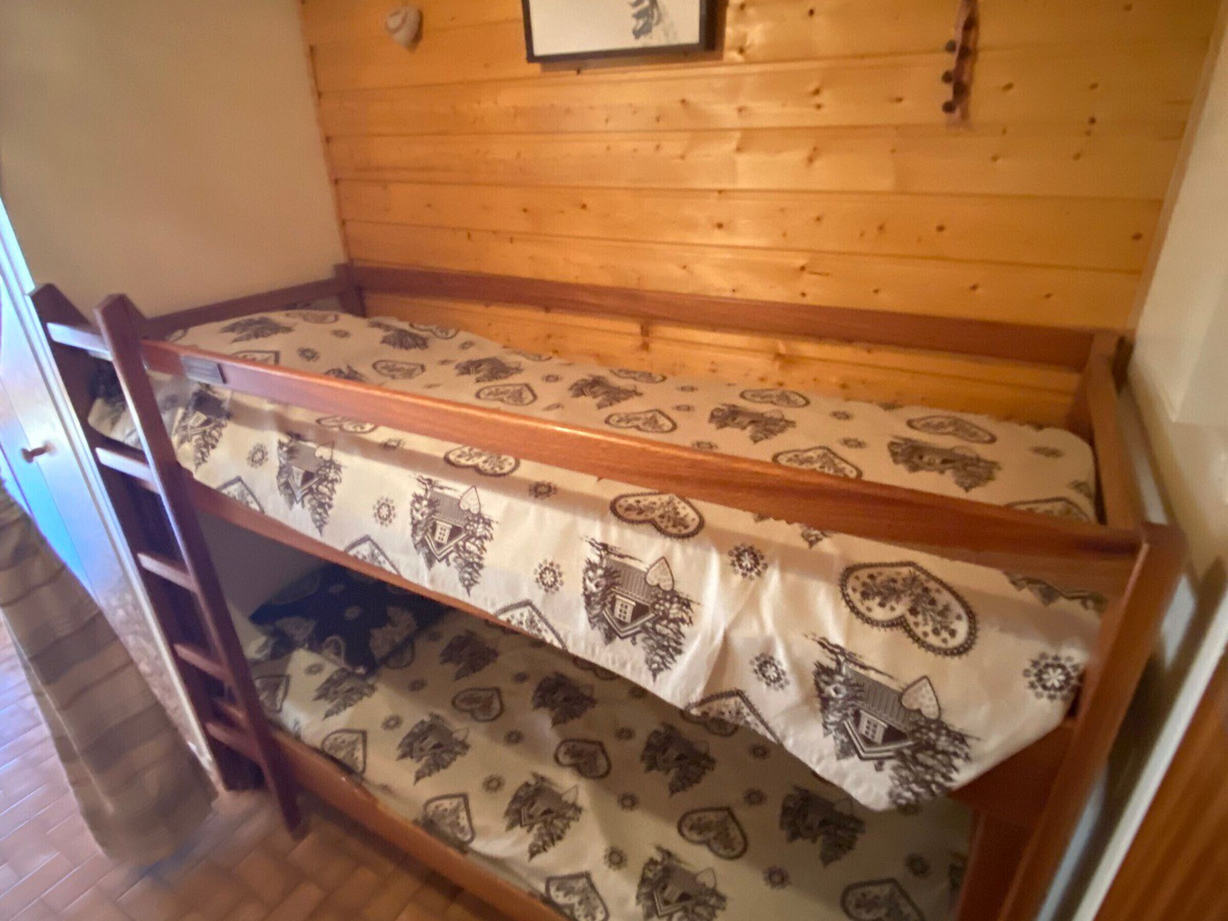 A bunk bed with patterned bedding in a room with wooden walls and a door.
